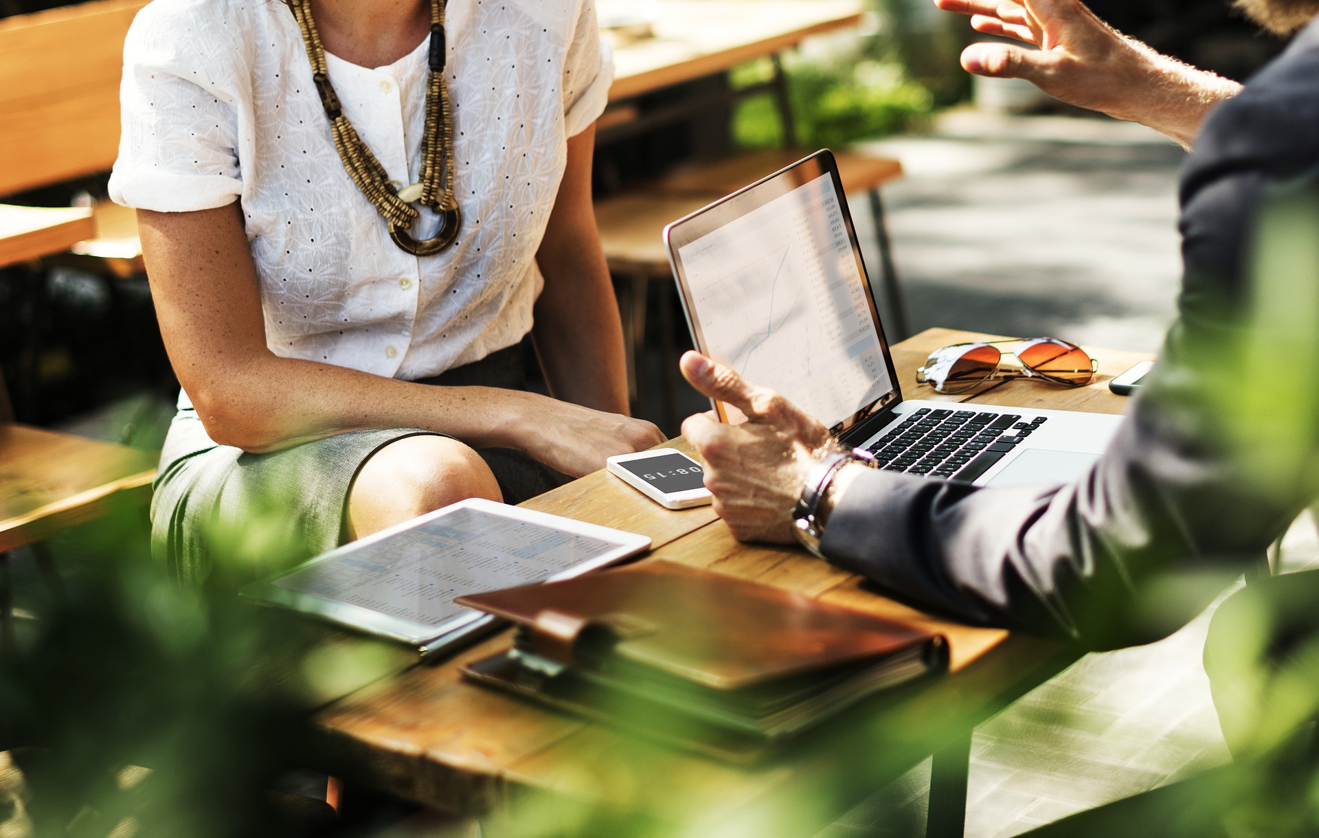 A man in a business suit sits at a table with a laptop and a woman in business clothes across from him as they share professional real estate advice.