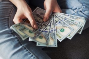 A pair of hands holds a handful of money fanned out in their palms for payment & cost of owning an investment property