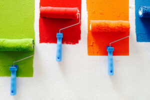 4 paint rollers on a wall with green, red, orange, and blue paint