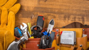 A set of tools and worker gloves for property maintenance on a hardwood floor.