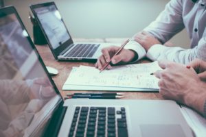 A property manager and a landlord sit at a desk with two laptops while looking over financial reporting on a rental lease. We offer residential property management services and real estate investment services in Kelowna BC.