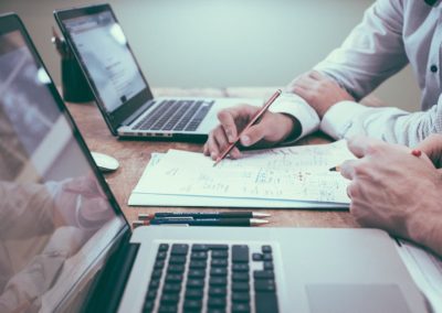 A property manager and a landlord sit at a desk with two laptops while looking over financial reporting on a rental lease. We offer residential property management services and real estate investment services in Kelowna BC.