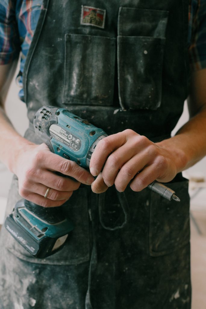 A contractor holds a battery-powered screwdriver while working on repairs for a rental property as a contractor for investment property repairs & maintenance.