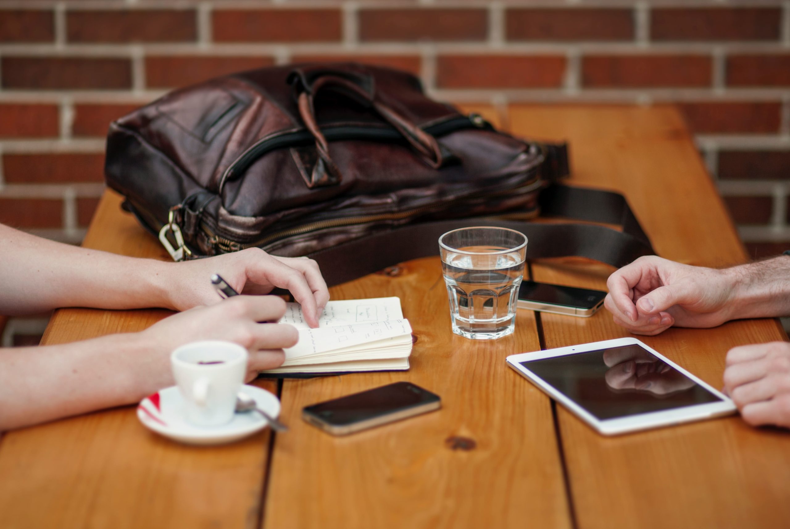 Two people sit at a cafe table with an espresso cup, glass of water, brief case and notes on the table as they perform Careful tenant screening for a Kelowna rental.