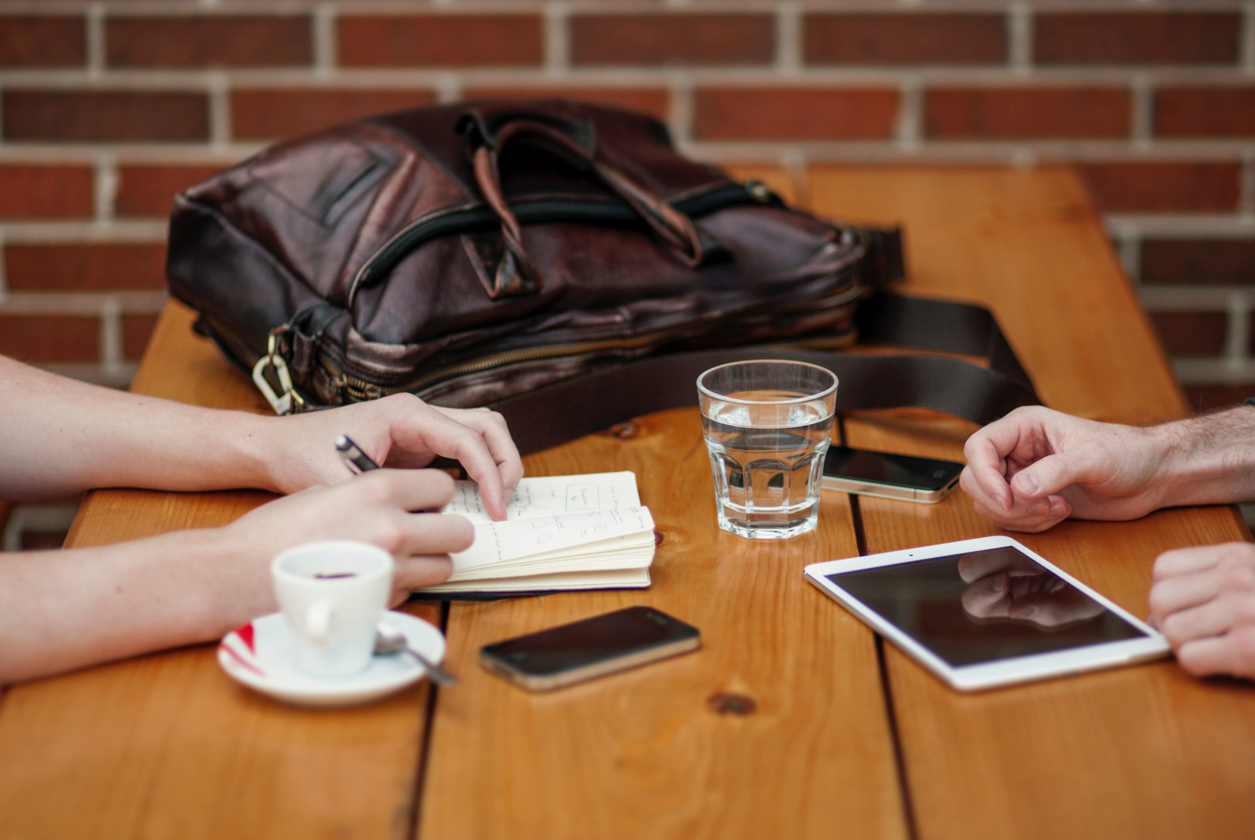 Two people sit at a cafe table with an espresso cup, glass of water, brief case and notes on the table as they perform Careful tenant screening for a Kelowna rental.