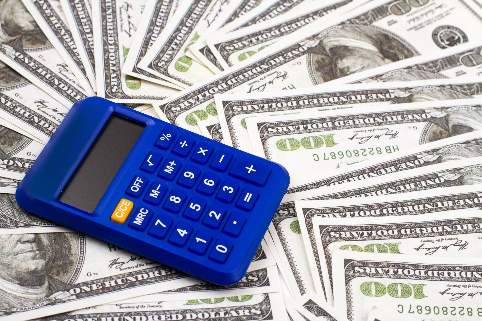 A blue calculator lays on top of a pile of 100 dollar bills. Consider Money