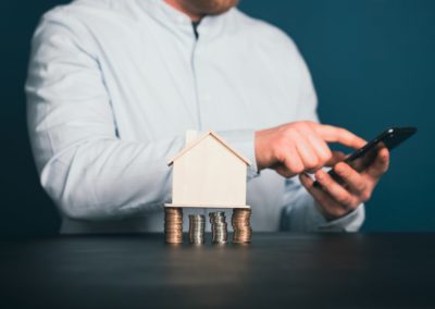 A mini fake house on top of piled up coins with a homeowner in the background looking at their phone. With the right manager, your investment can go further.