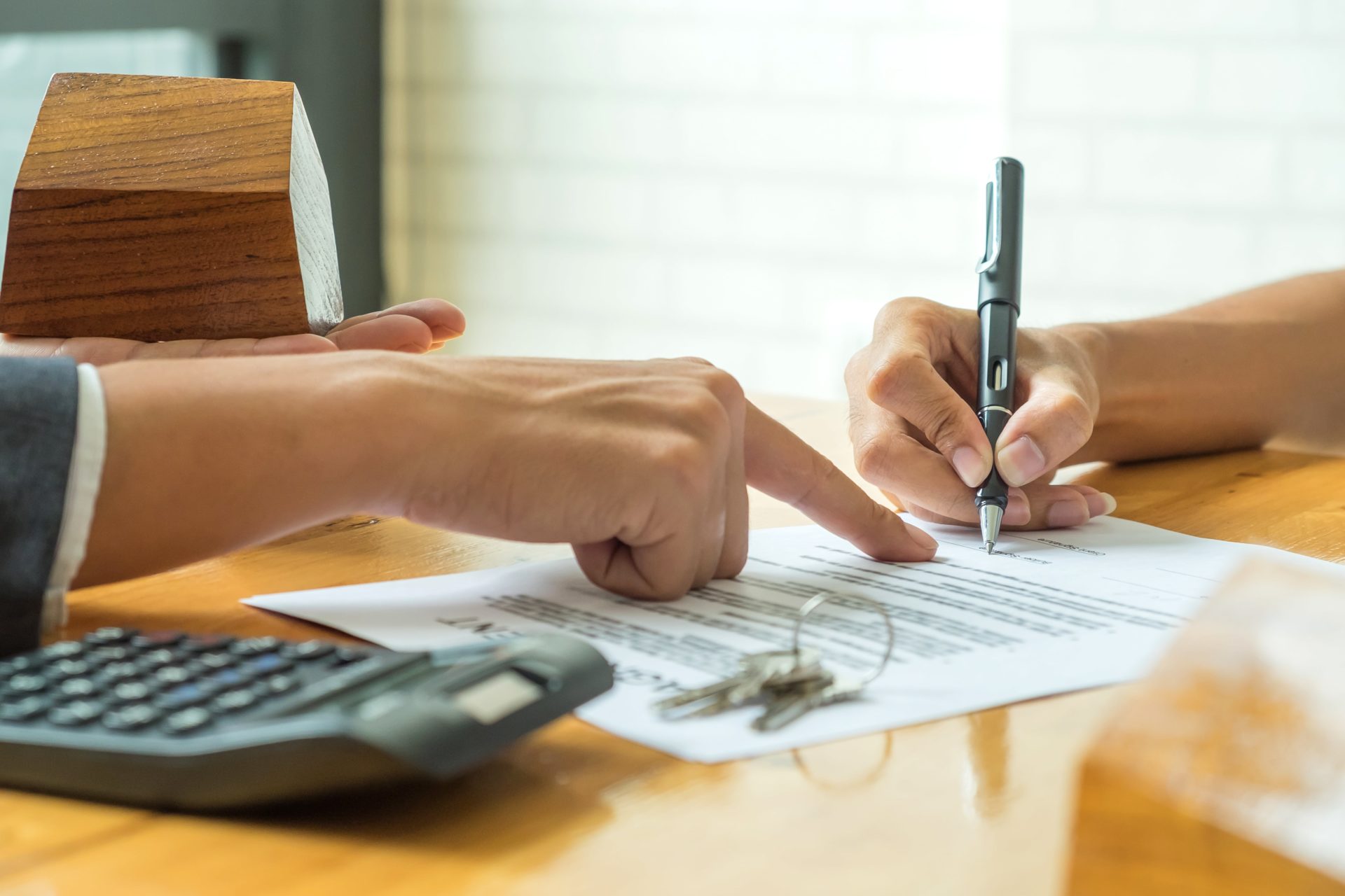 A view of two pairs of hands as one signs a Lease Agreement while the other, the landlord or property manager, points at the document.