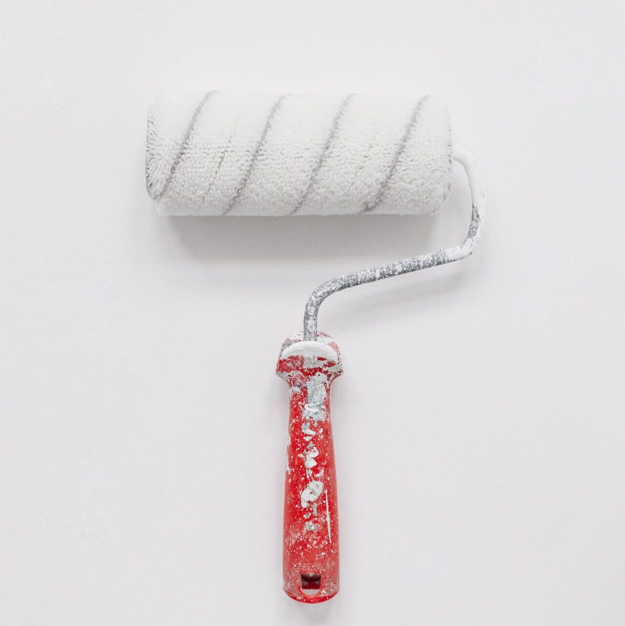 A paint roll with a red handle covered with white paint lying on a white background.