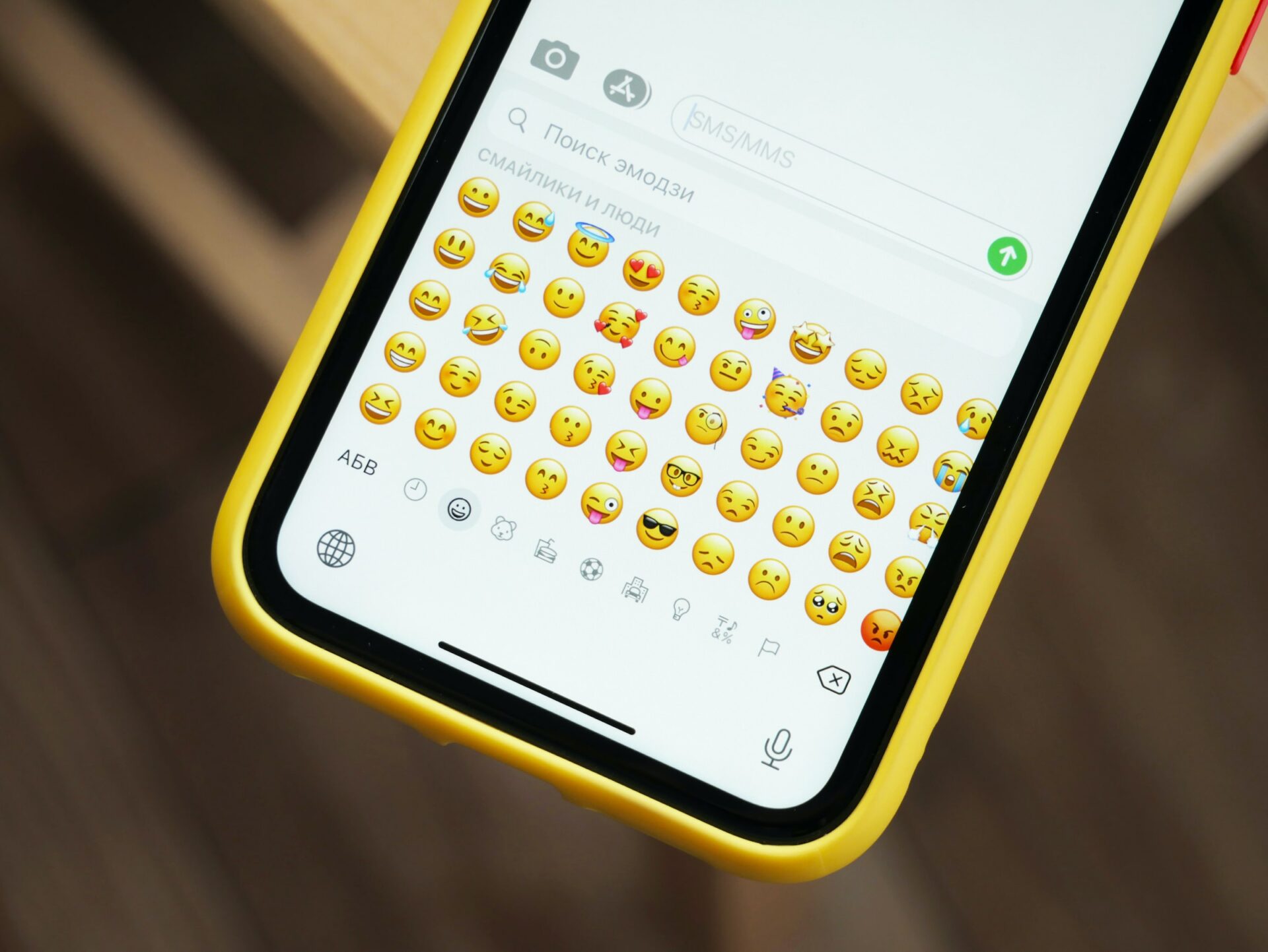 A close up of an apple iphone cellphone in a bright yellow case, with different emoji options opened in a text message.