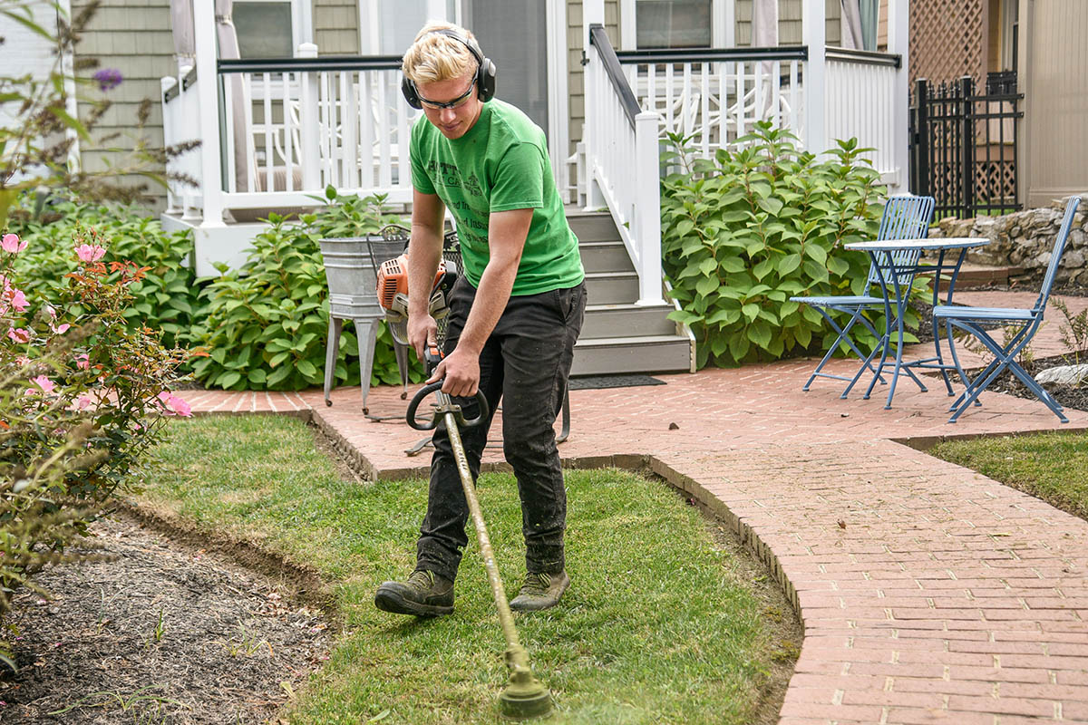 A man weed whacking the front yard of a rental home