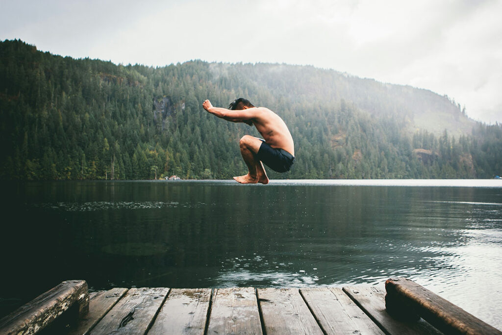 A man jumping into a lake from a dock in the summer